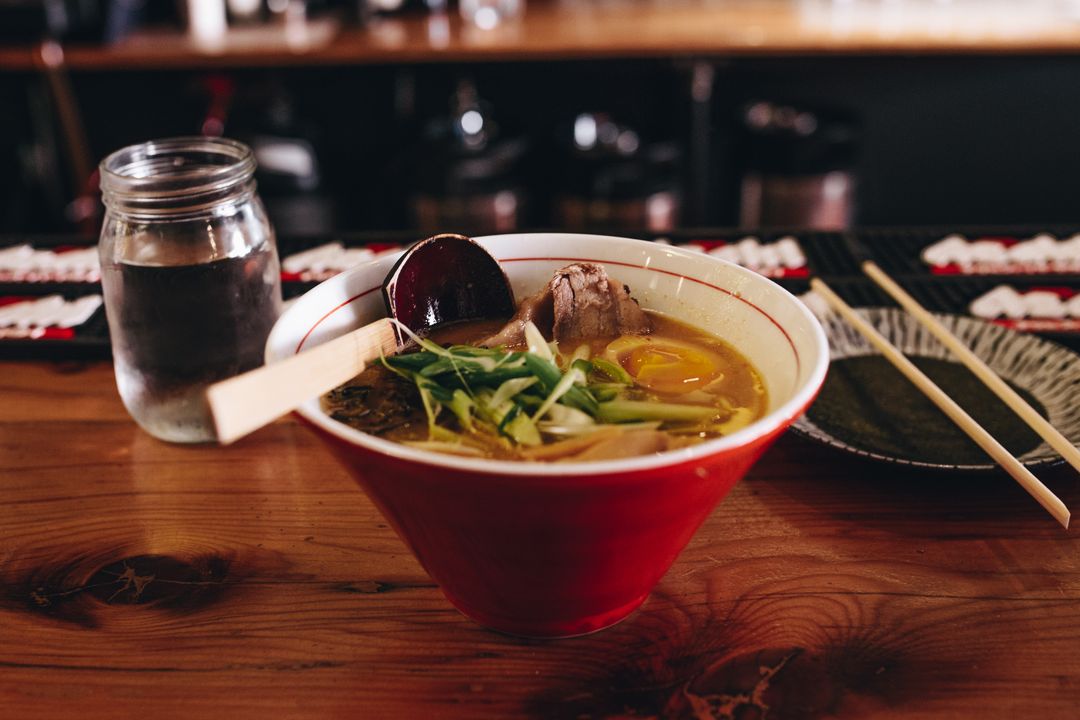 Steaming ramen bowl with soft-boiled egg, sliced chashu pork and greens on wooden counter