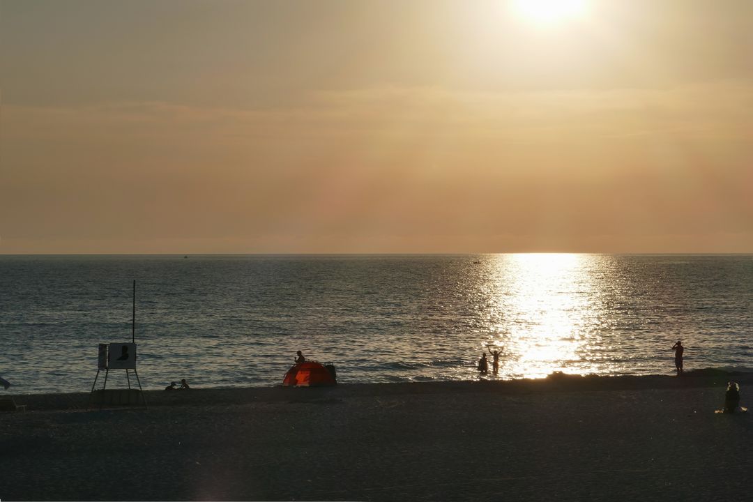Sunset Over Tranquil Beach with Silhouetted Figures and Tent - Free Images, Stock Photos and Pictures on Pikwizard.com