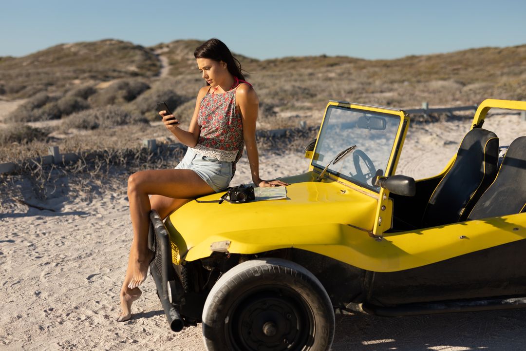 Caucasian woman sitting on beach buggy with camera and map, using smartphone on sunny beach - Free Images, Stock Photos and Pictures on Pikwizard.com