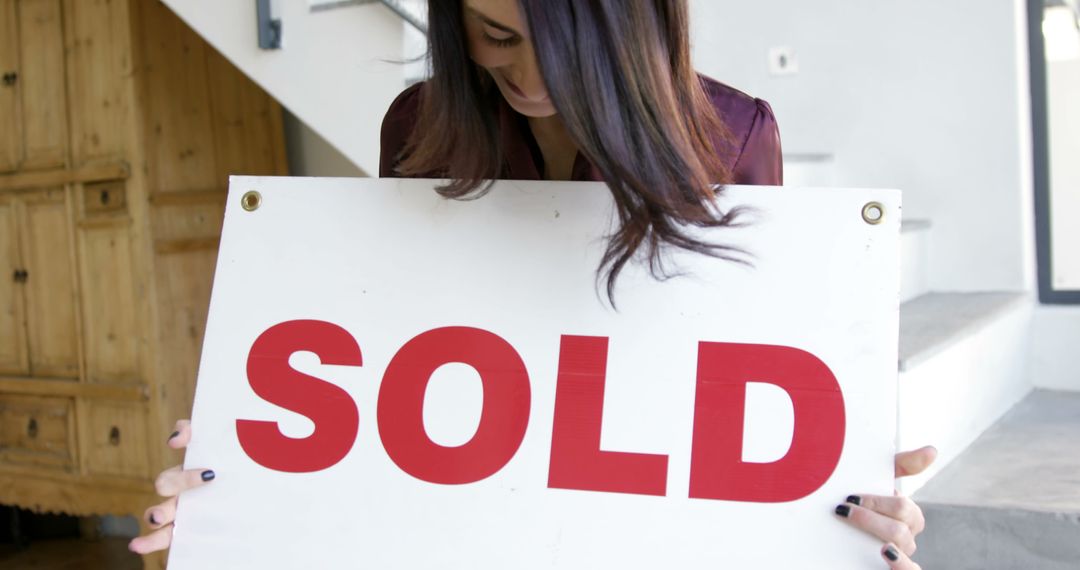 Joyful woman holding SOLD sign in new home - Free Images, Stock Photos and Pictures on Pikwizard.com