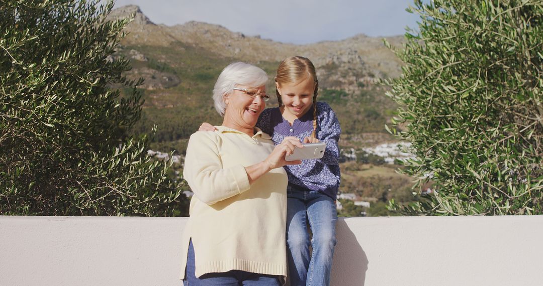 Grandmother and Granddaughter Smiling While Looking at Smartphone Outdoors - Free Images, Stock Photos and Pictures on Pikwizard.com