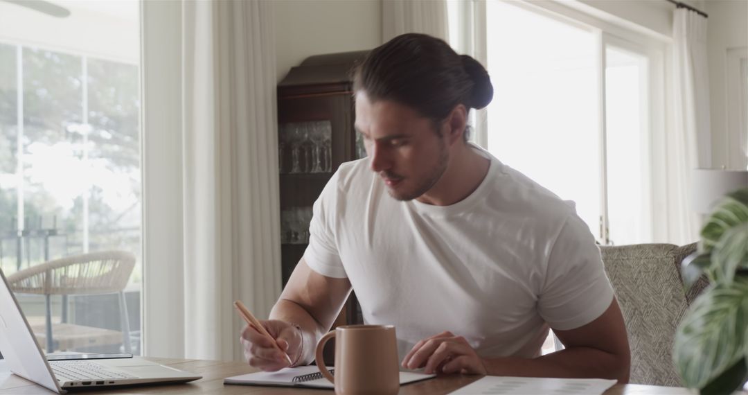Focused Young Man Working on Laptop with Notepad and Coffee