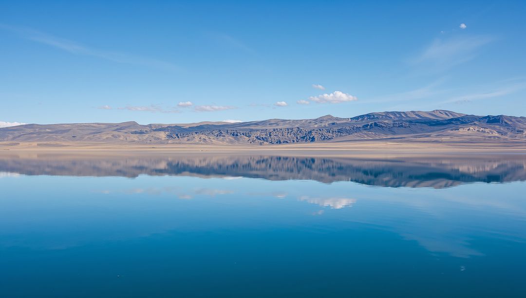 Glassy High-Plain Lake Reflecting Rolling Hills and Clear Blue Sky in Minimalist Panorama