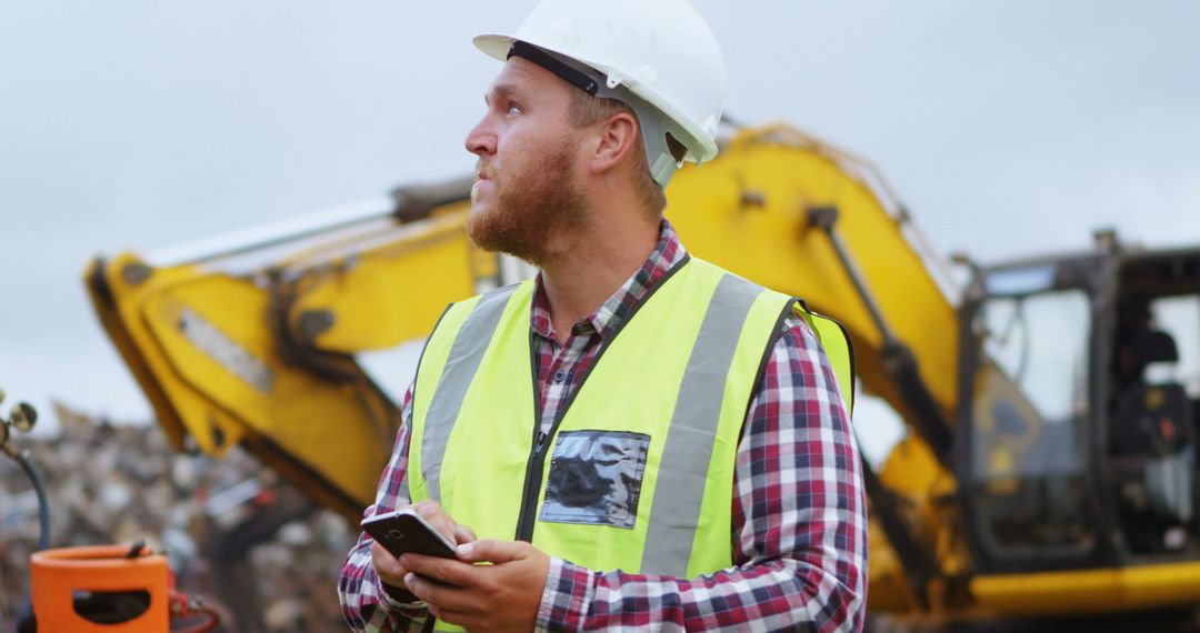 Construction Worker Using Smartphone at Job Site with Excavator in Background - Free Images, Stock Photos and Pictures on Pikwizard.com