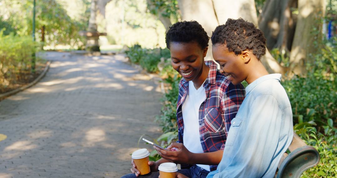 Happy Twin Sisters Using Smartphone Outdoors With Coffee