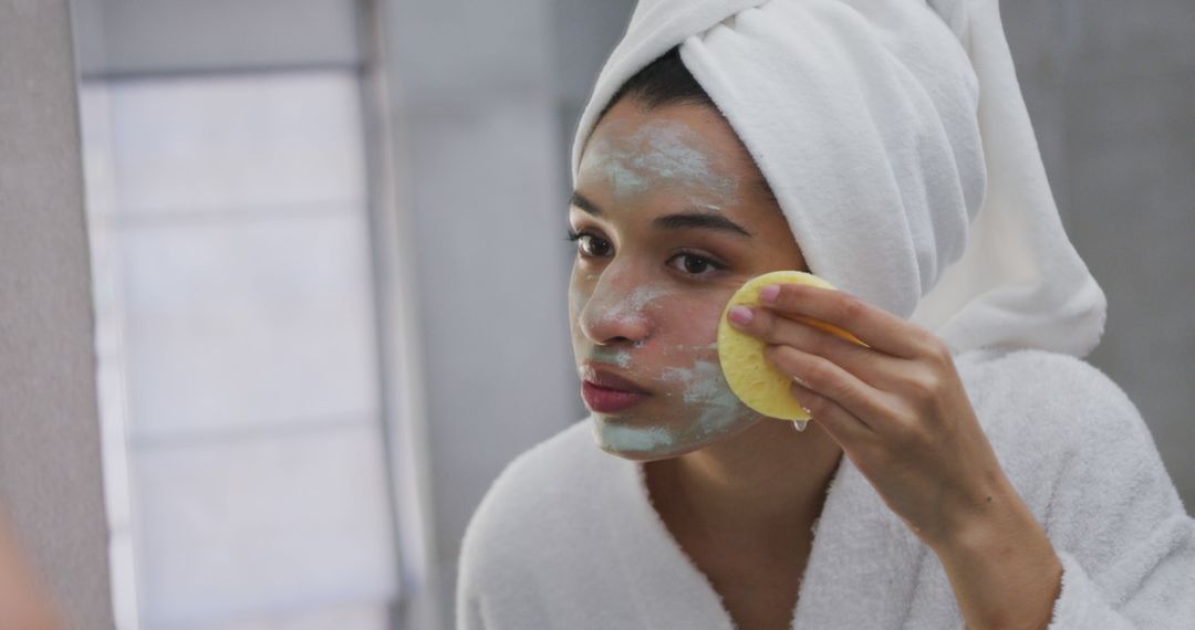 Biracial woman removing face mask in bathroom, wearing bathrobe - Free Images, Stock Photos and Pictures on Pikwizard.com