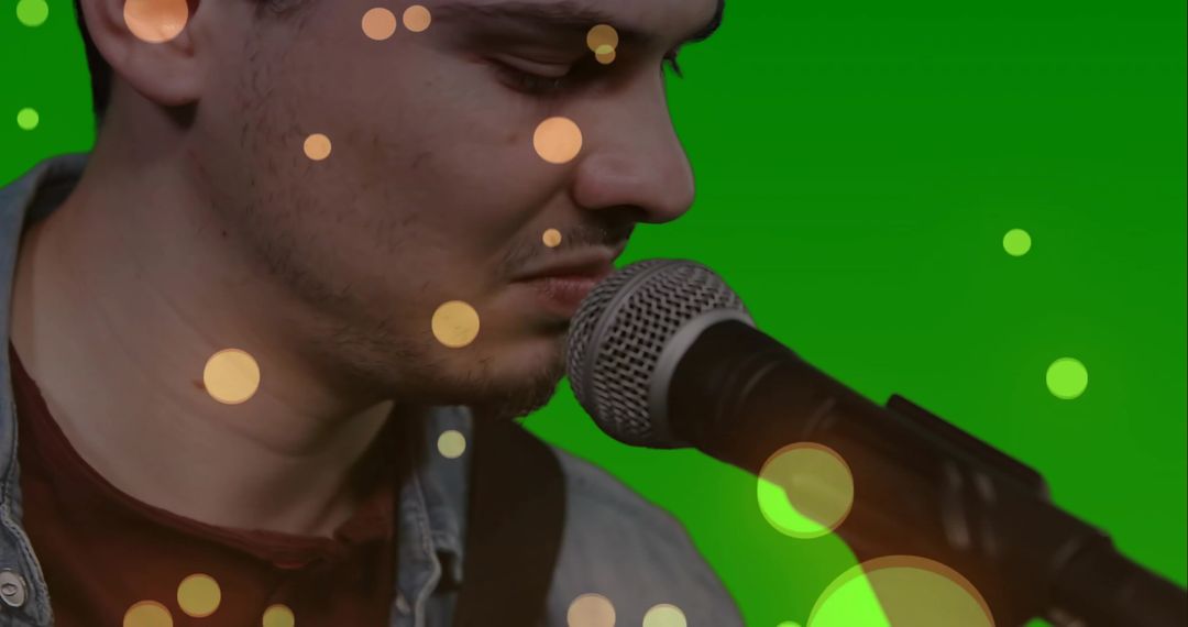 Male Vocalist Leaning Into Microphone Singing Over Emerald Backdrop with Warm Bokeh