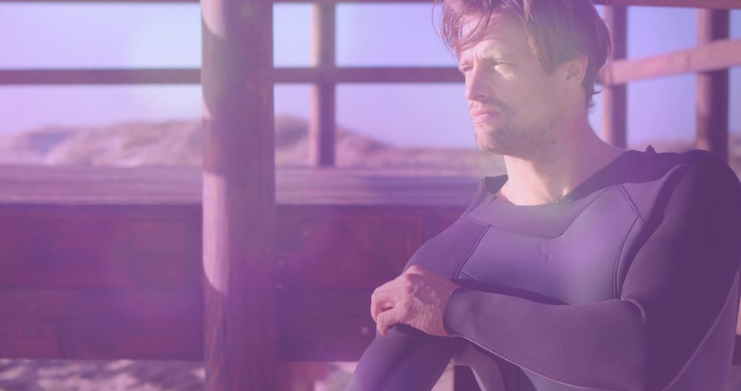 Man Adjusting Wetsuit on Deck Overlooking Sandy Dunes