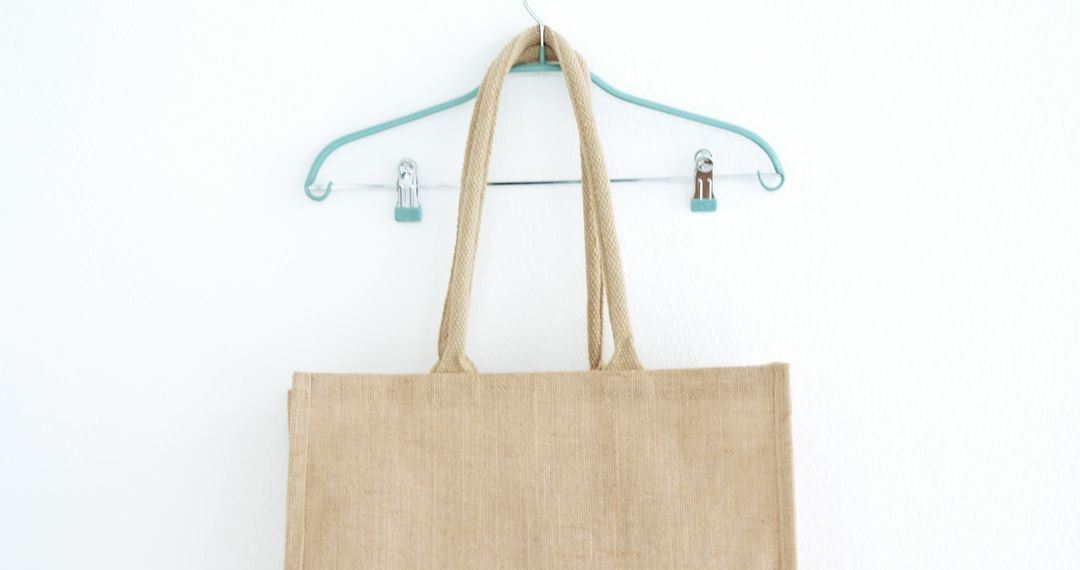 A beige tote bag hangs on a light blue hanger against a white wall, with copy space - Free Images, Stock Photos and Pictures on Pikwizard.com