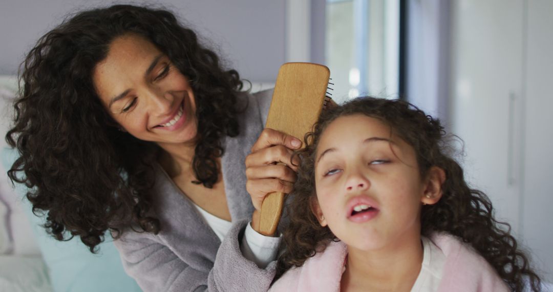 Mother combing daughter's curly hair with wooden brush - Free Images, Stock Photos and Pictures on Pikwizard.com
