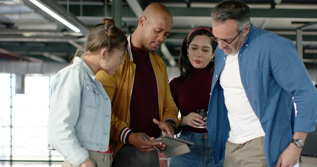 Diverse team collaborating around tablet using stylus and coffee in modern open-plan office