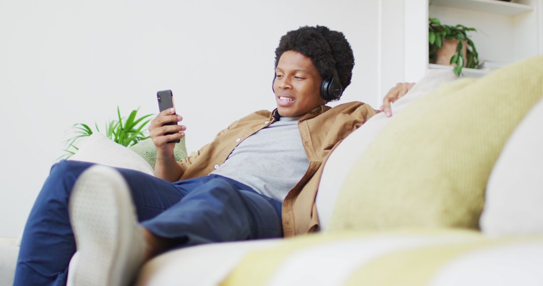 Young Smiling Man Relaxing at Home with Smartphone and Headphones