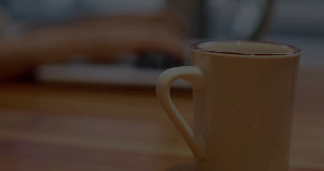 Cozy workspace with speckled ceramic mug sitting near blurred laptop keyboard and hands