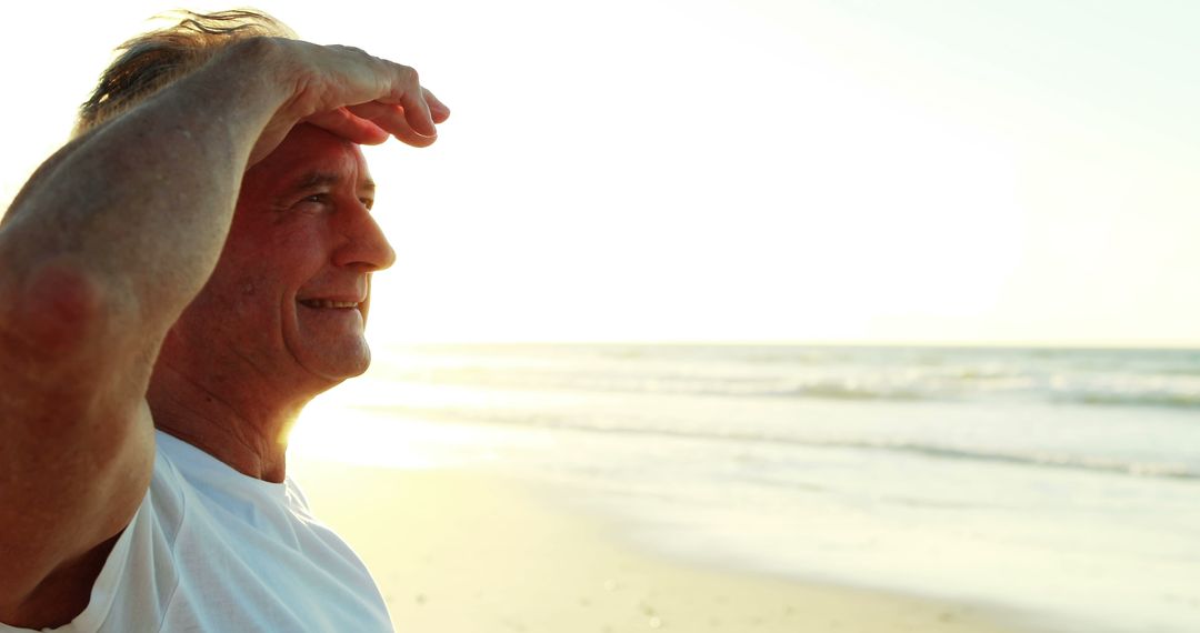 Man smiling in sunlight on serene beach, looking into distance - Free Images, Stock Photos and Pictures on Pikwizard.com