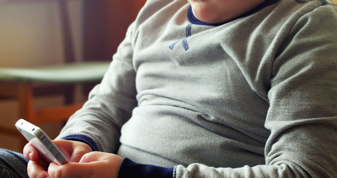 Child Using Smartphone Indoors Wearing Gray Sweater - Free Images, Stock Photos and Pictures on Pikwizard.com