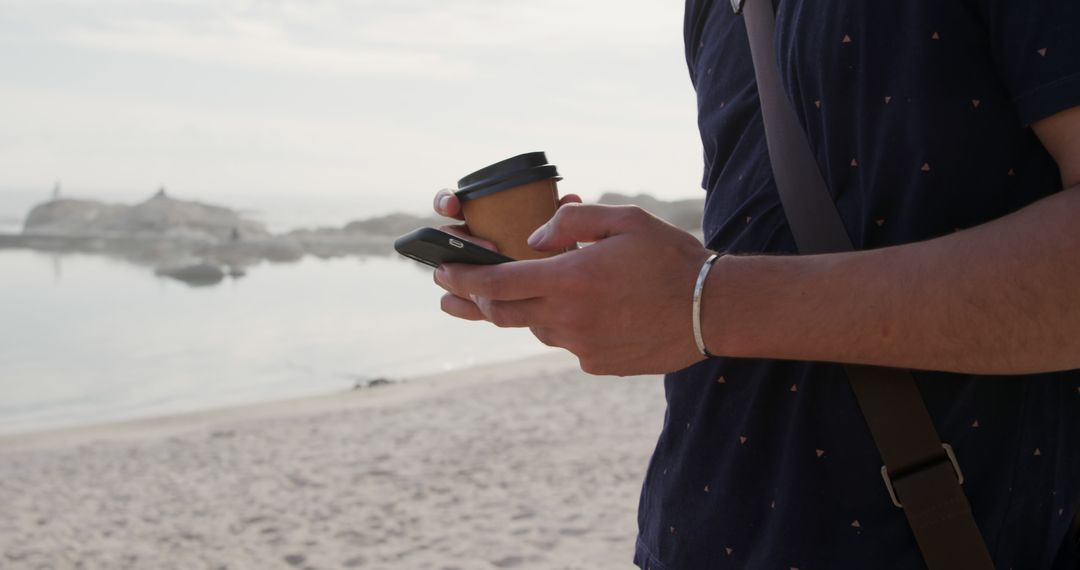 Person Holding Coffee and Smartphone at Beach - Free Images, Stock Photos and Pictures on Pikwizard.com