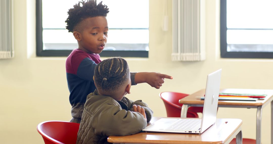 Boys Collaborating on Laptop in Classrooms with Red Chairs
