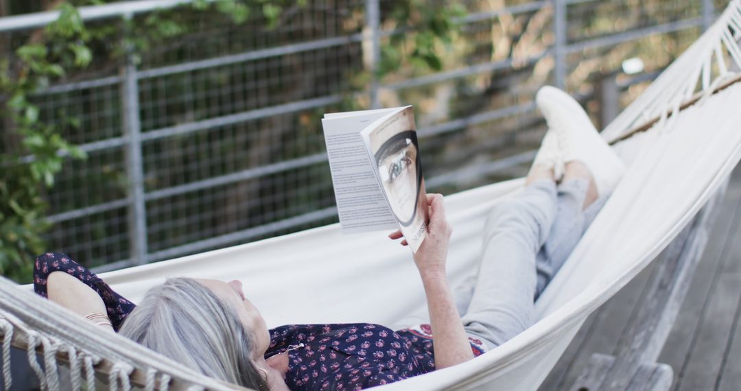 Relaxed Senior Woman Reading a Book in a Hammock Outdoors - Free Images, Stock Photos and Pictures on Pikwizard.com