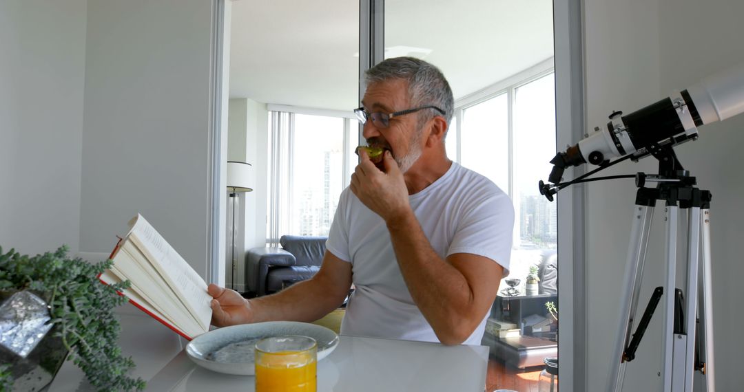 Middle-Aged Man Reading Book While Eating Sandwich at Home