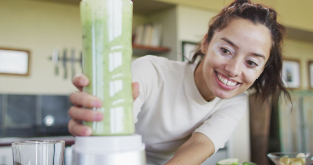 Smiling Woman Making Green Smoothie with Blender in Modern Kitchen