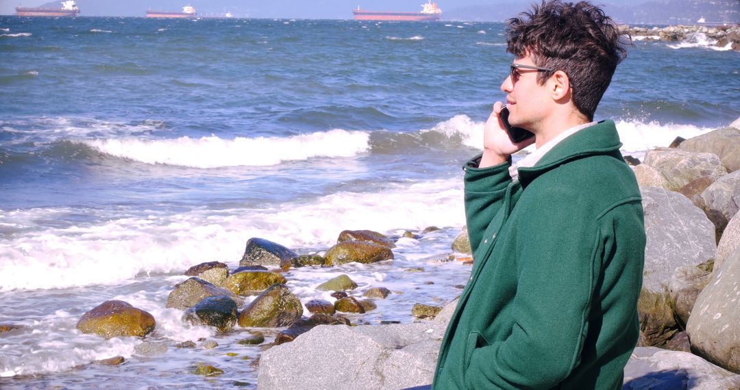 Young Man Talking On Phone Near Sea With Ships In Background - Free Images, Stock Photos and Pictures on Pikwizard.com