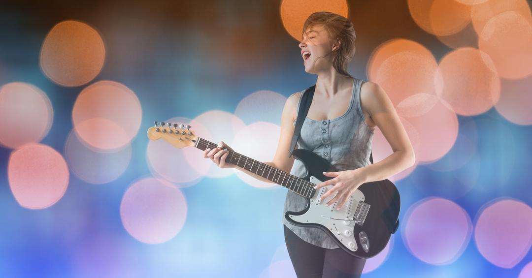 Female music artist playing guitar while singing over bokeh - Free Images, Stock Photos and Pictures on Pikwizard.com
