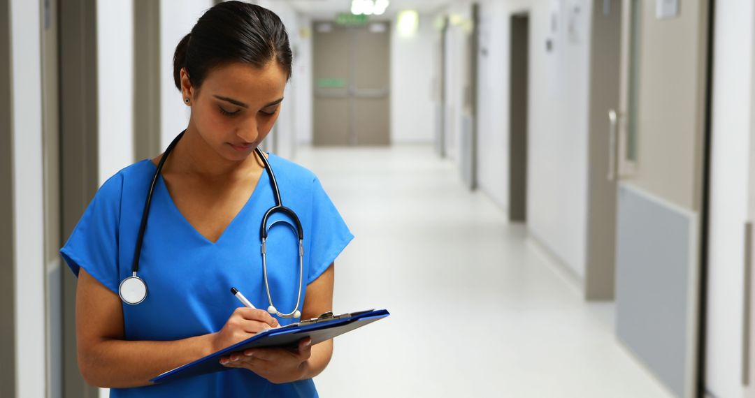 Female healthcare worker writing patient notes in hospital corridor - Free Images, Stock Photos and Pictures on Pikwizard.com