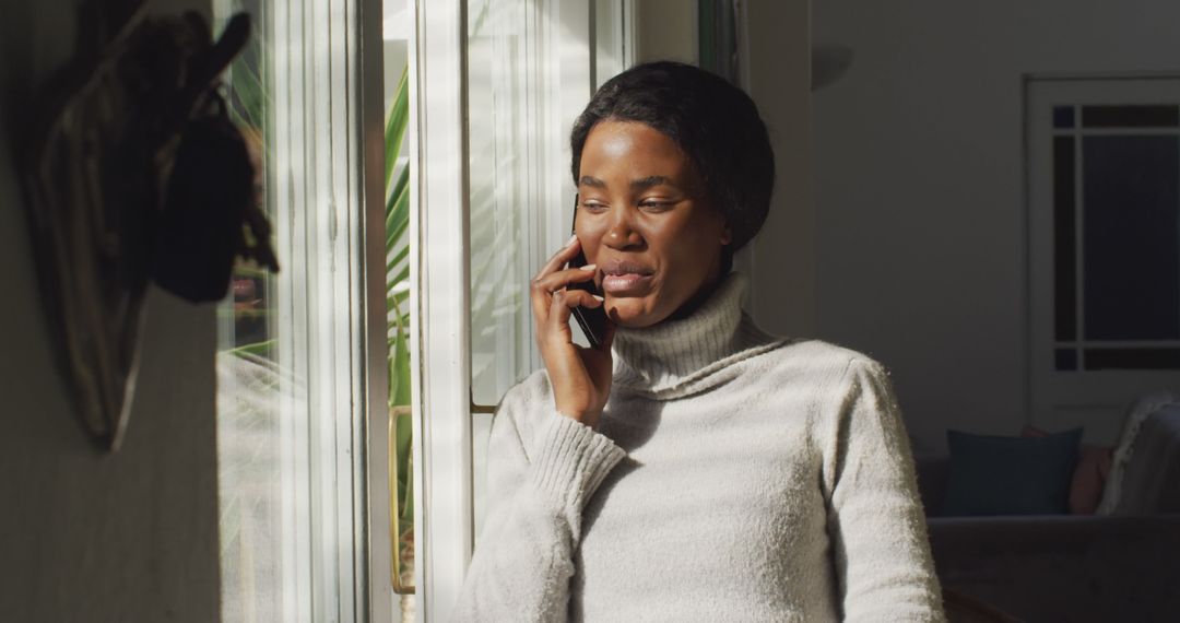 Afro-Caribbean Woman Talking on Smartphone Near Sunlit Window - Free Images, Stock Photos and Pictures on Pikwizard.com