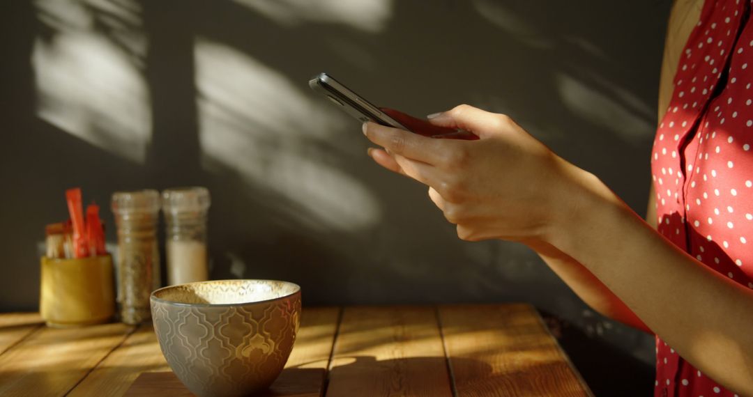 Woman Using Smartphone in Sunlit Kitchen with Coffee Mug - Free Images, Stock Photos and Pictures on Pikwizard.com