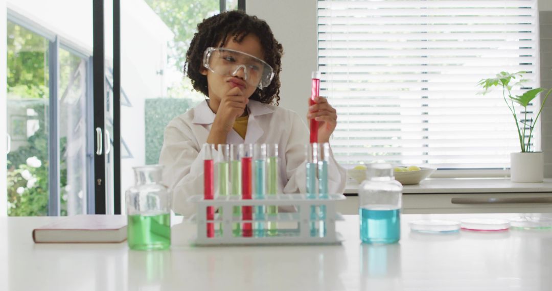 Young scientist experimenting with colorful test tubes on bright kitchen counter