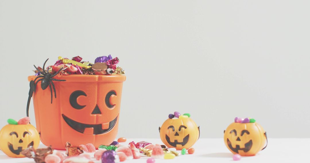 Halloween Pumpkin Bucket Overflowing With Candy, Smiling Jack-o-Lantern Faces and Spider