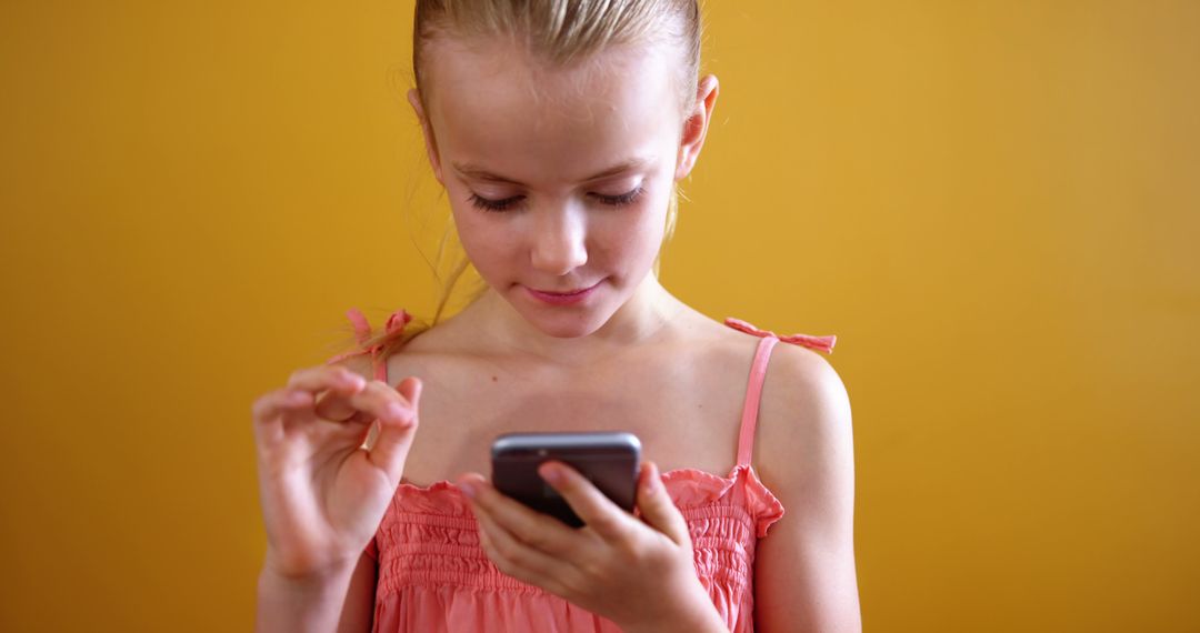 Young Schoolgirl Engaged with Smartphone Against Yellow Background - Free Images, Stock Photos and Pictures on Pikwizard.com