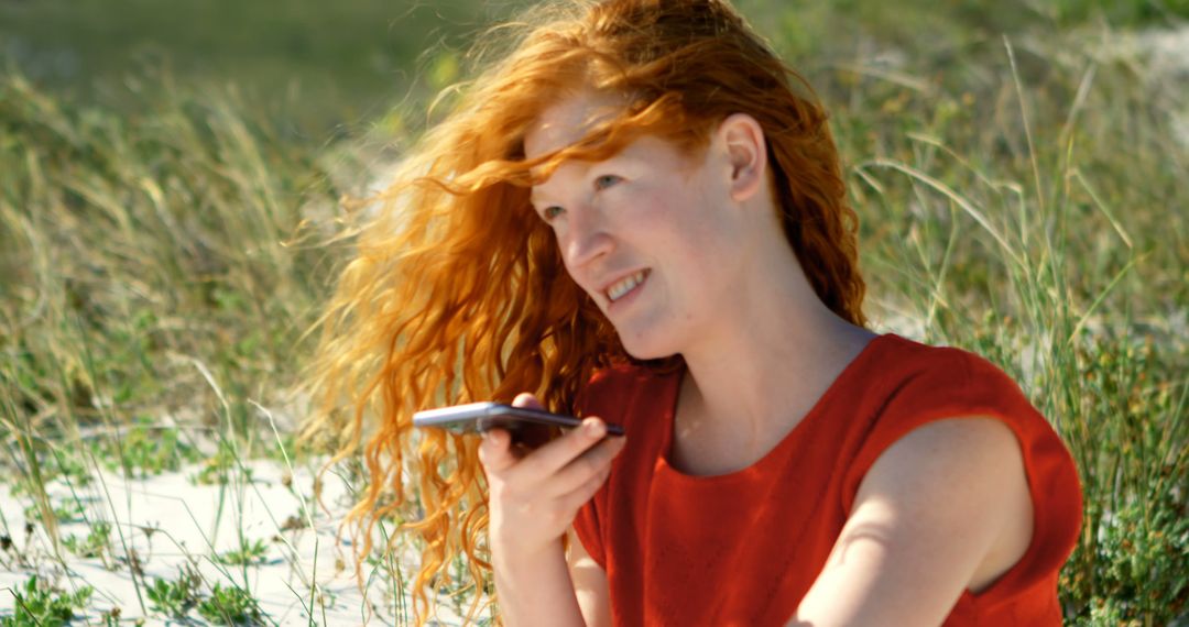 Red-haired woman using smartphone on a sunny beach - Free Images, Stock Photos and Pictures on Pikwizard.com