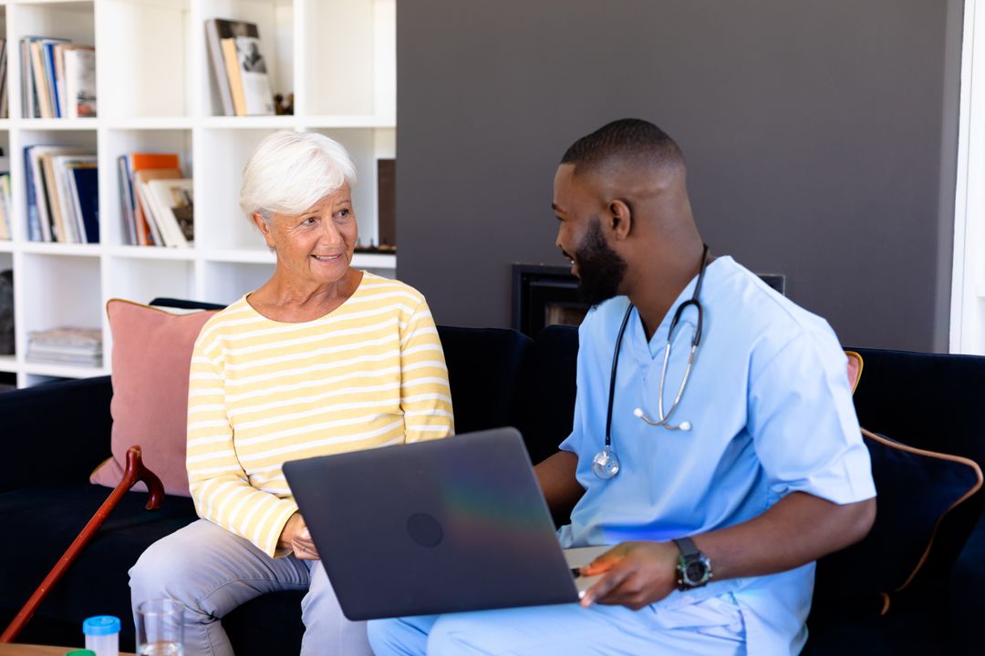Black male doctor with laptop discusses with elderly biracial woman on sofa - Free Images, Stock Photos and Pictures on Pikwizard.com