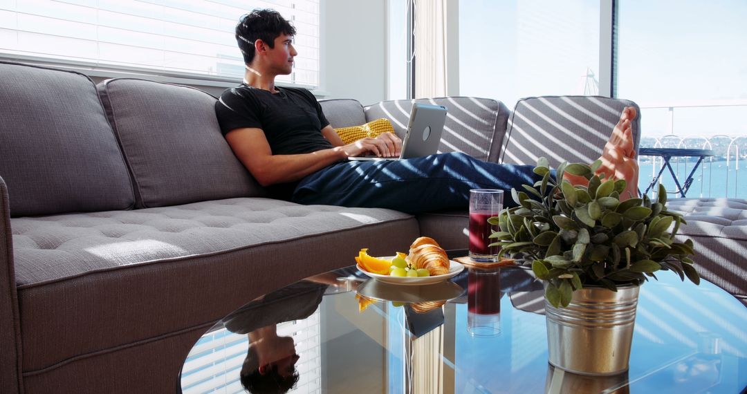 Young Man Relaxing on Sofa with Laptop in Bright Modern Living Room - Free Images, Stock Photos and Pictures on Pikwizard.com