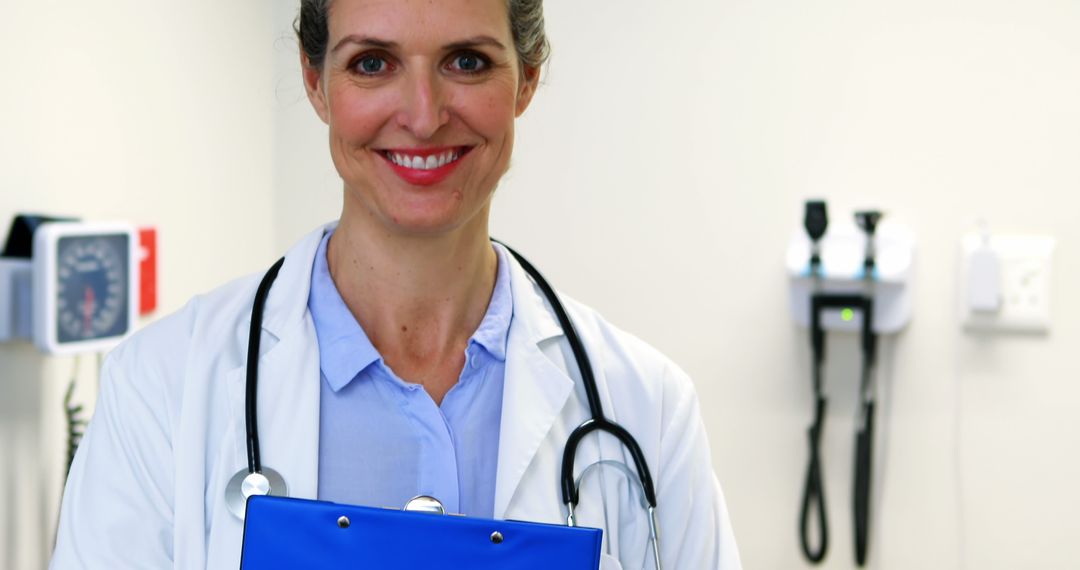 Cheerful Female Doctor Holding Blue Clipboard in Medical Office - Free Images, Stock Photos and Pictures on Pikwizard.com