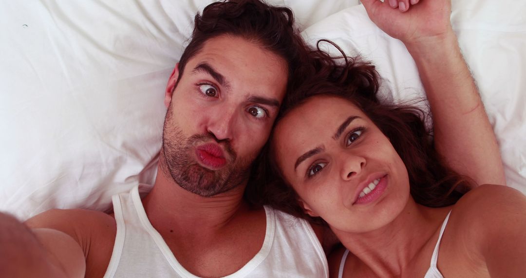 Playful couple taking selfie in bed making funny faces - Free Images, Stock Photos and Pictures on Pikwizard.com