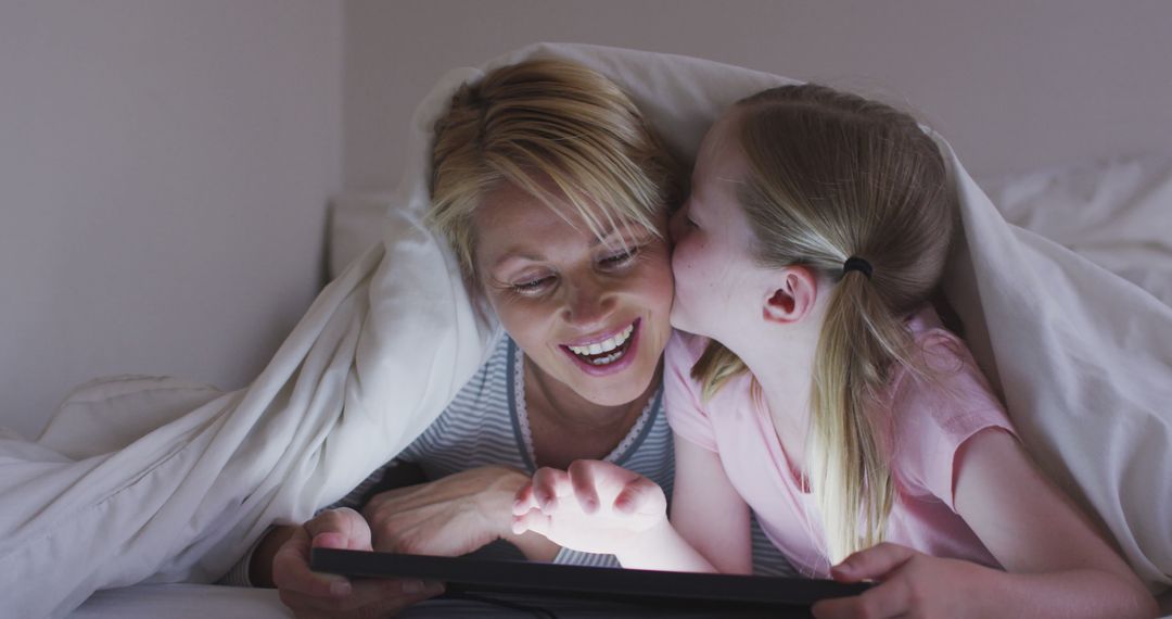 Happy caucasian mother with daughter kissing her and using tablet together under duvet in bed - Free Images, Stock Photos and Pictures on Pikwizard.com