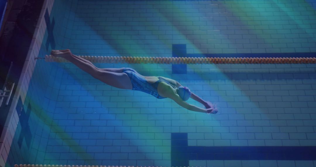 Competitive swimmer gliding underwater along lane rope in illuminated Olympic-style pool