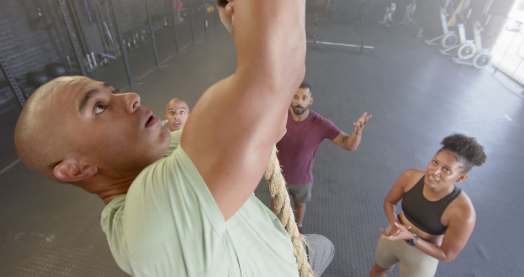 Group Encouraging Man Climbing Rope in Gym - Free Images, Stock Photos and Pictures on Pikwizard.com