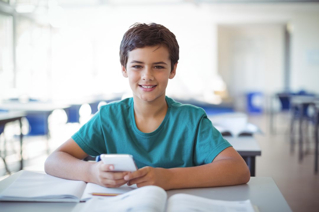Schoolboy Using Smartphone in Bright Classroom with Books