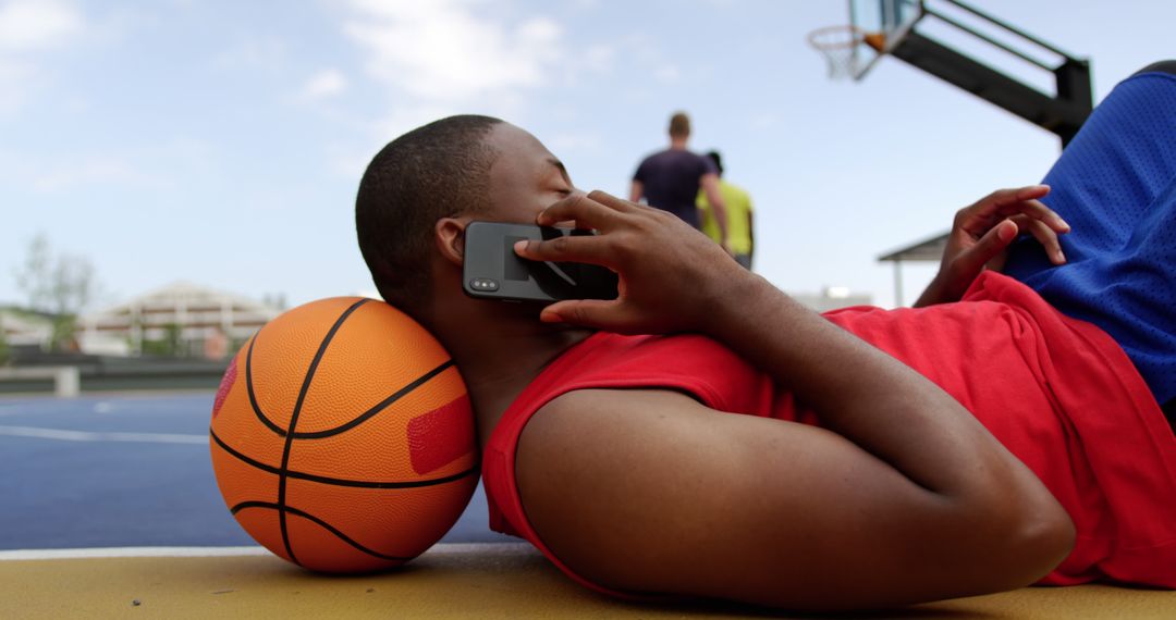 Young Man Talking on Smartphone While Relaxing on Outdoor Basketball Court - Free Images, Stock Photos and Pictures on Pikwizard.com