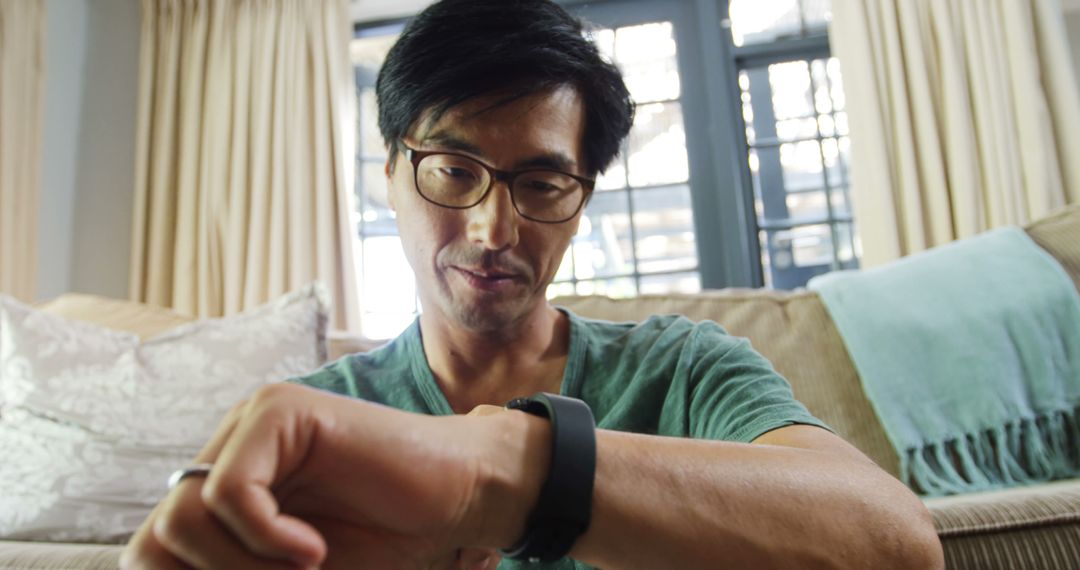 Asian Man Checking Fitness Tracker Sitting on Couch - Free Images, Stock Photos and Pictures on Pikwizard.com