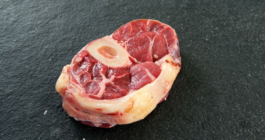 A raw beef shank with a visible marrow bone is placed on a dark textured surface, with copy space - Free Images, Stock Photos and Pictures on Pikwizard.com