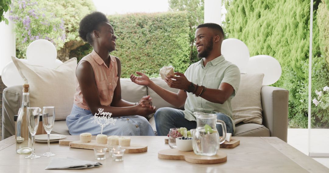 Joyful Couple Exchanging Gifts on Patio Seating with Refreshments