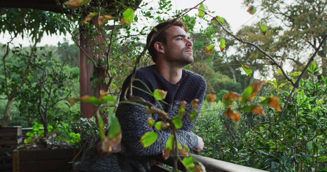 Man Reflecting on Wooden Balcony Surrounded by Lush Greenery - Free Images, Stock Photos and Pictures on Pikwizard.com