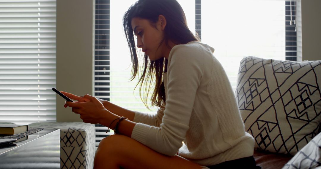 Young woman relaxing with smartphone on sofa in modern living room - Free Images, Stock Photos and Pictures on Pikwizard.com