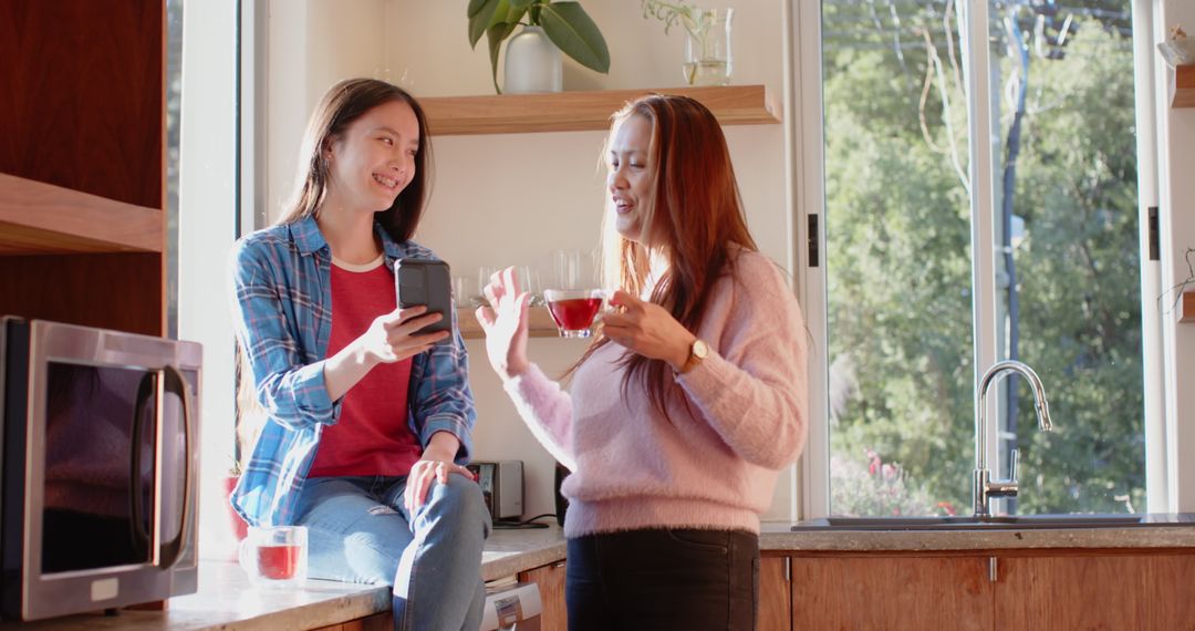 Asian Mother and Daughter Enjoying Tea and Conversation in Cozy Kitchen
