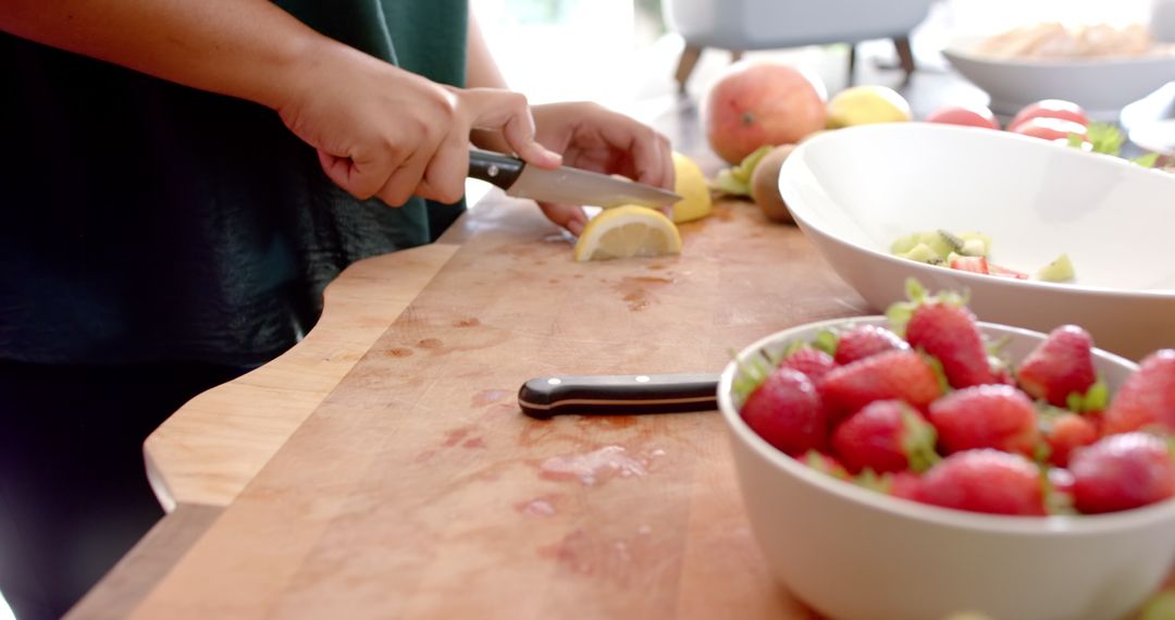 Person Cutting Lemon Slices for Fresh Fruit Salad Preparation