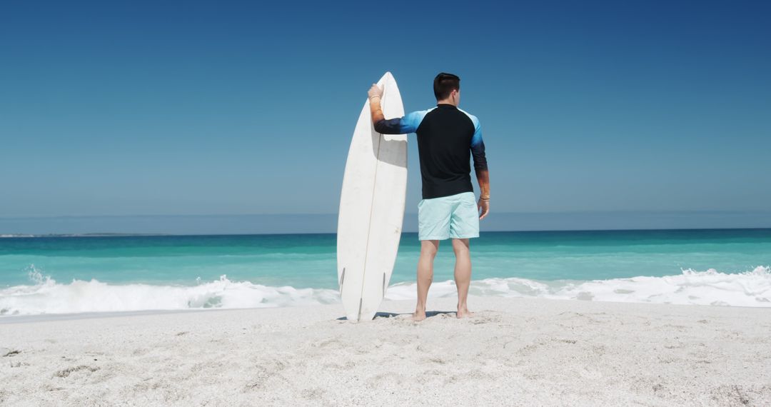 Man Holding Surfboard on Sandy Beach Under Clear Blue Sky - Free Images, Stock Photos and Pictures on Pikwizard.com